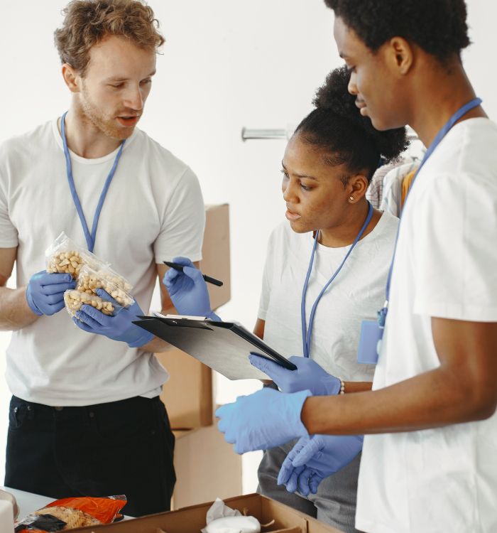 Three people wearing gloves and white shirts looking at a clipboard.