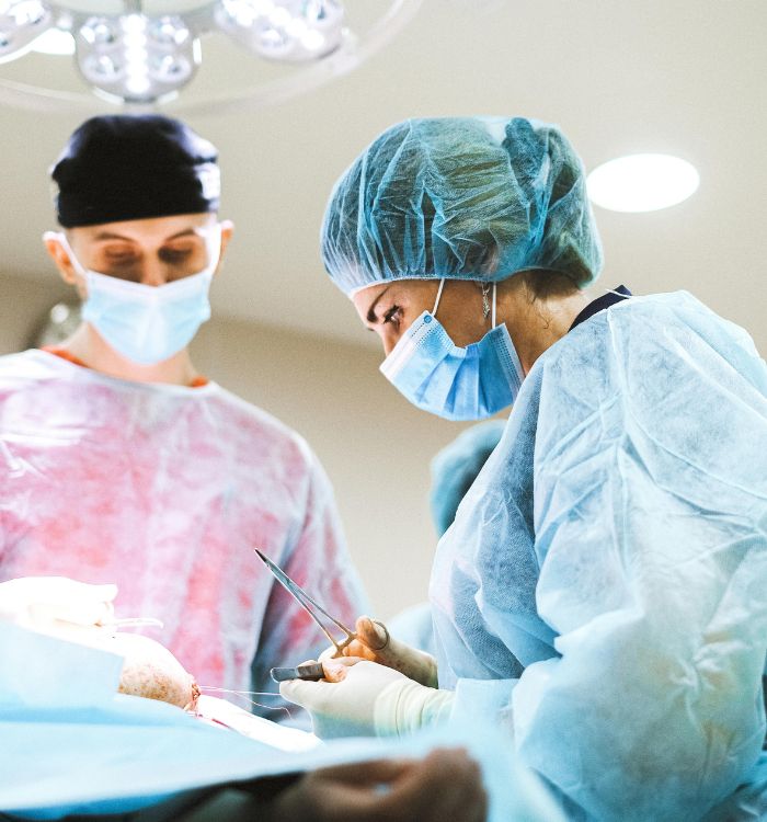 A woman in a blue hat and a man in a red hat are working on a patient.