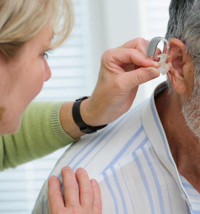 A woman is putting ear plugs in a man's ears.