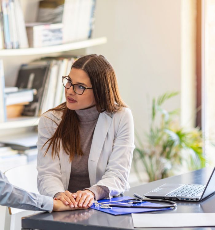 A woman in a white coat sitting at a table with a laptop.