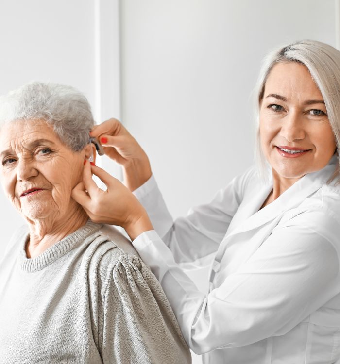 A woman in a white lab coat is adjusting a hearing aid.