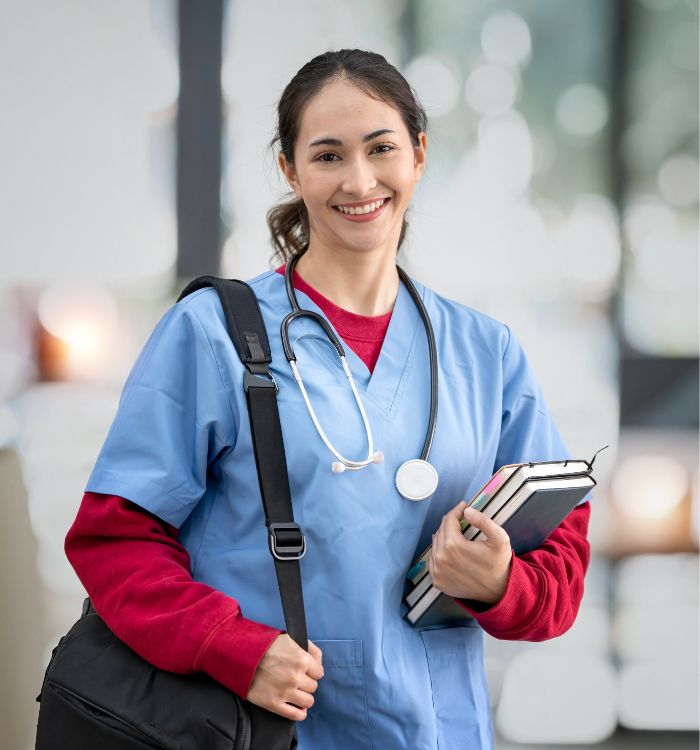 A woman in a blue shirt and red sweater holding a bag and a book.