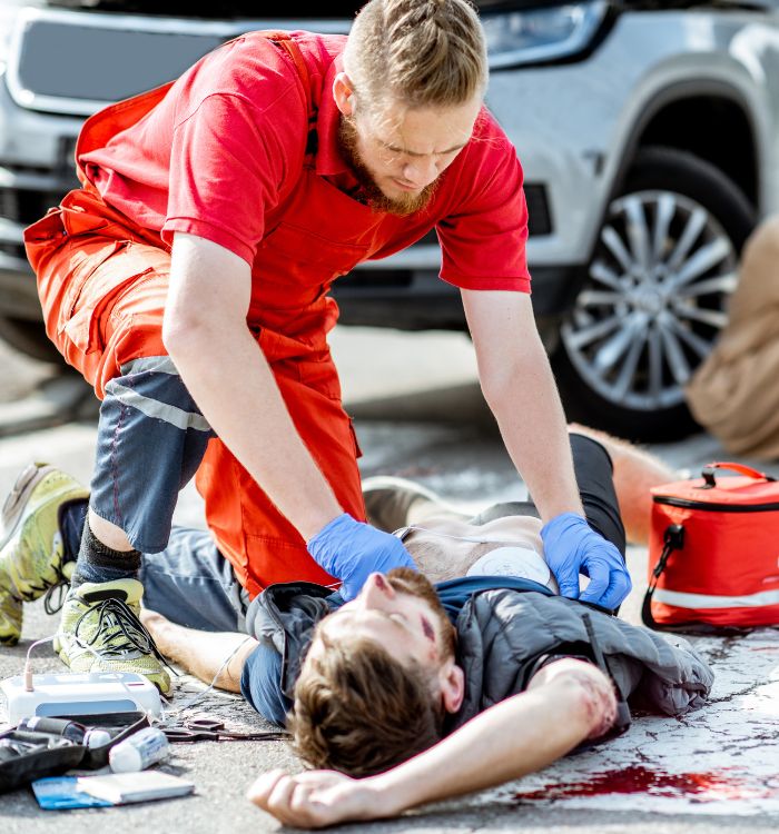 A man is lying on the ground with a man in a red shirt attending to him.