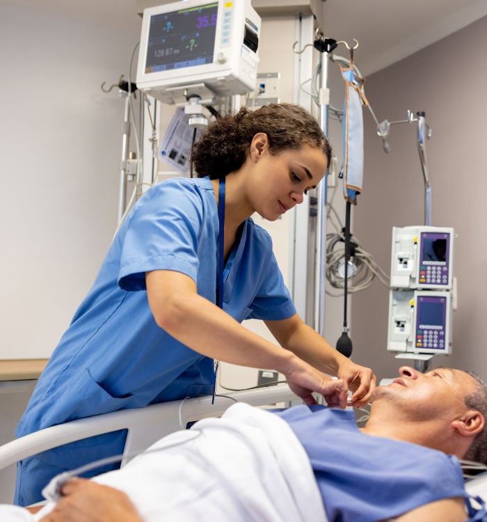 A woman in a blue dress is tending to a man in a hospital bed.