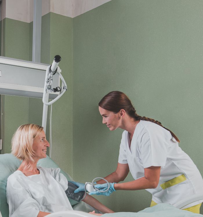 A woman in a white shirt is helping another woman with a blood pressure monitor.