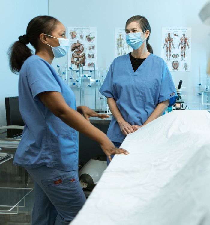Two women in scrubs standing in front of a table.