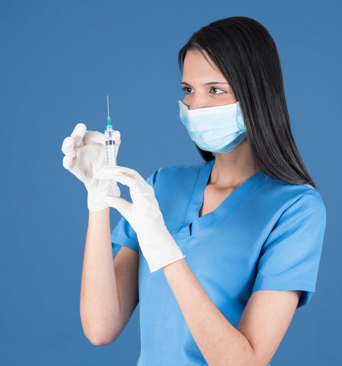 A woman wearing a blue shirt and gloves holding a syringe.