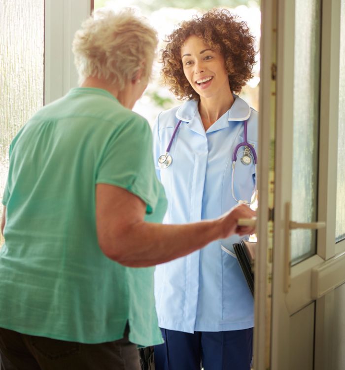 A woman in a blue shirt and white coat is smiling at a woman in a green shirt.