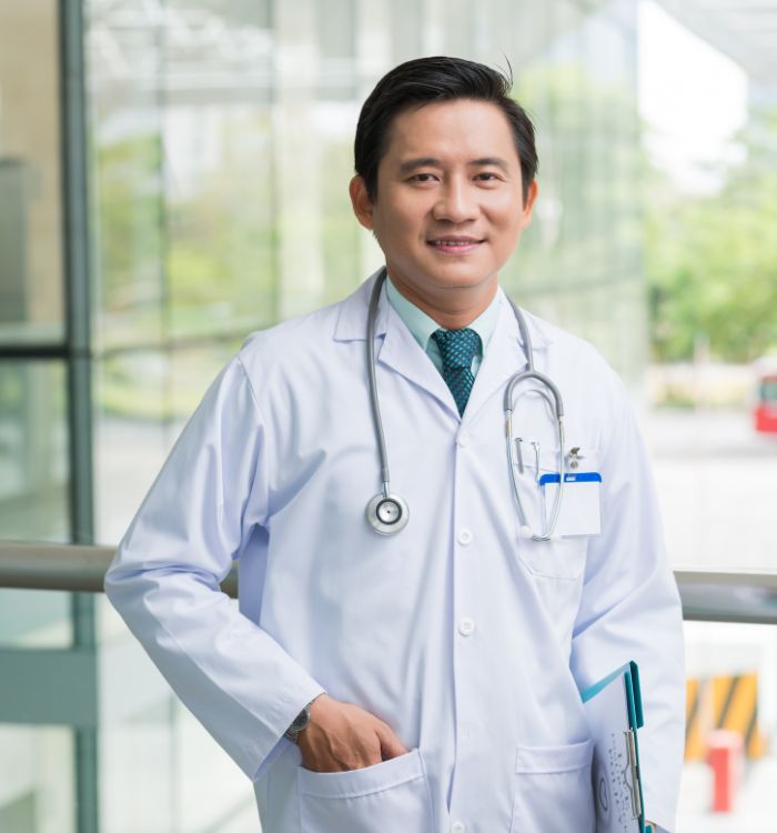 A man in a white coat and a green tie smiles for the camera.