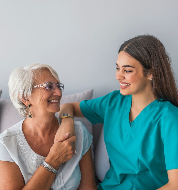 A woman in a white shirt and a woman in a blue shirt are smiling at each other.