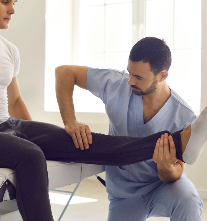A man in a white shirt is getting his knee worked on by a man in a blue shirt.