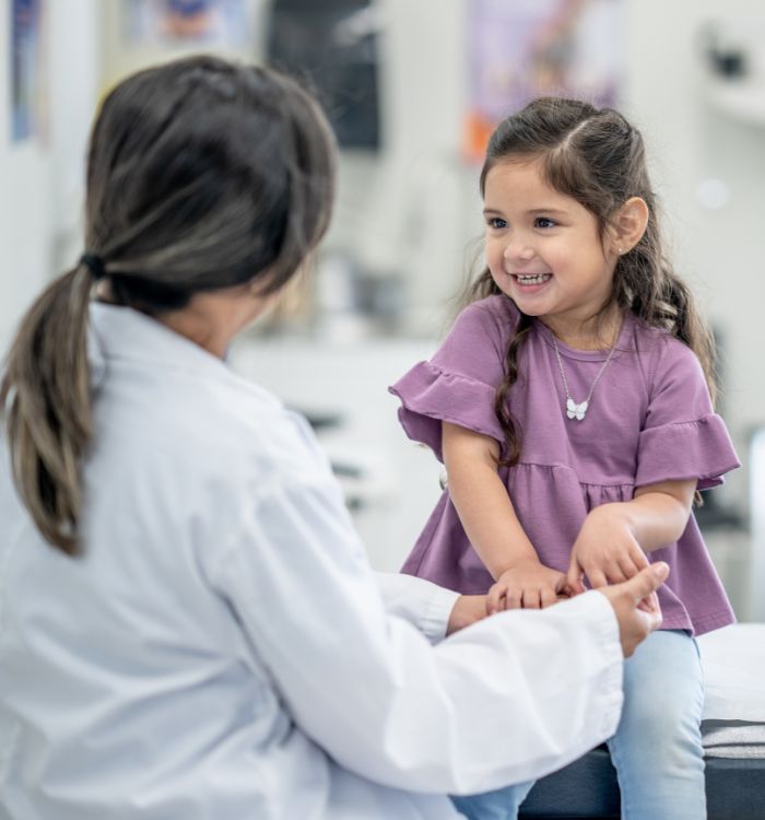 A woman in a white coat is holding a little girl's hands.