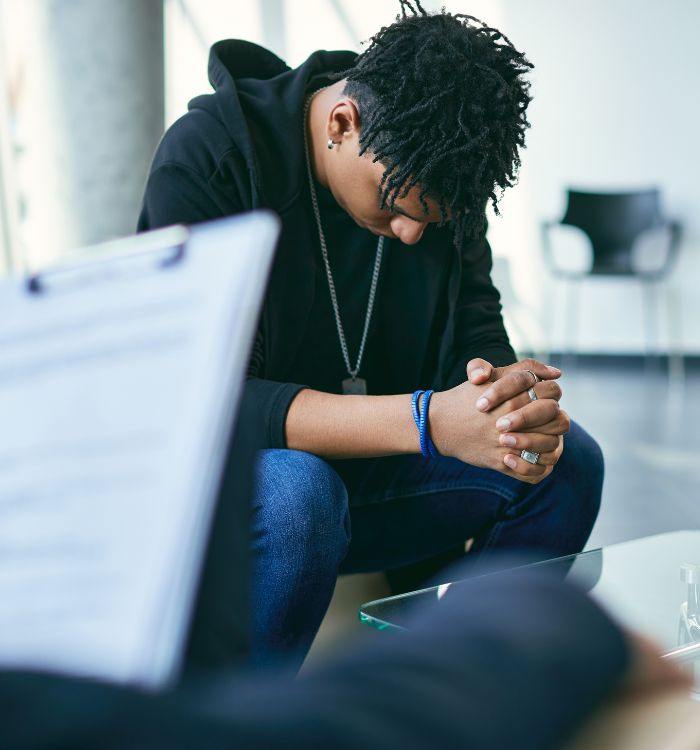 A man wearing a black hoodie and blue jeans is sitting in front of a clipboard.