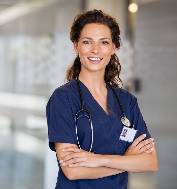 A woman in a blue shirt and a stethoscope standing in front of a glass wall.