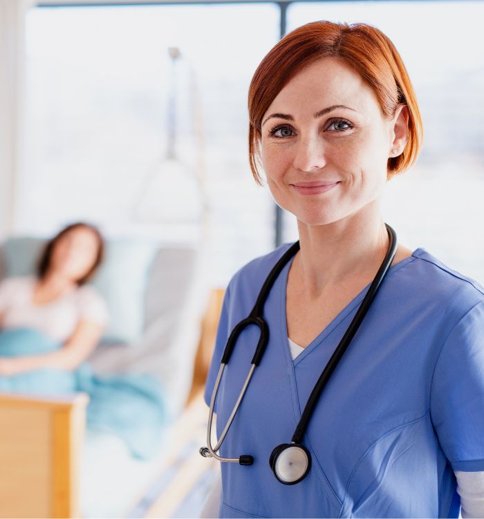A woman in a blue shirt and a stethoscope standing in a hospital room.
