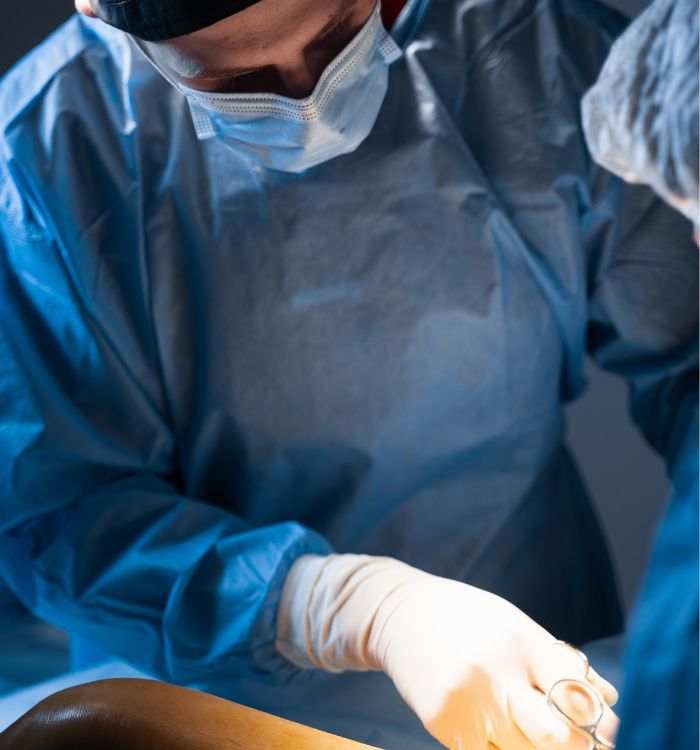 A surgeon wearing a blue gown and gloves is operating on a patient.