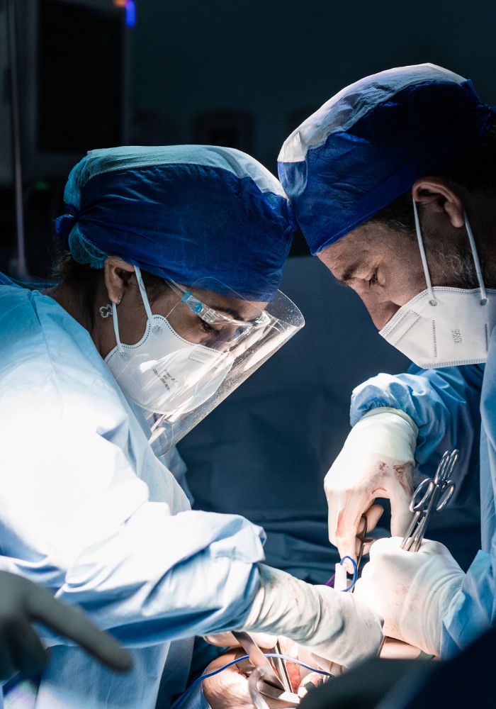 A man and woman wearing blue hats and gloves are working on a patient.