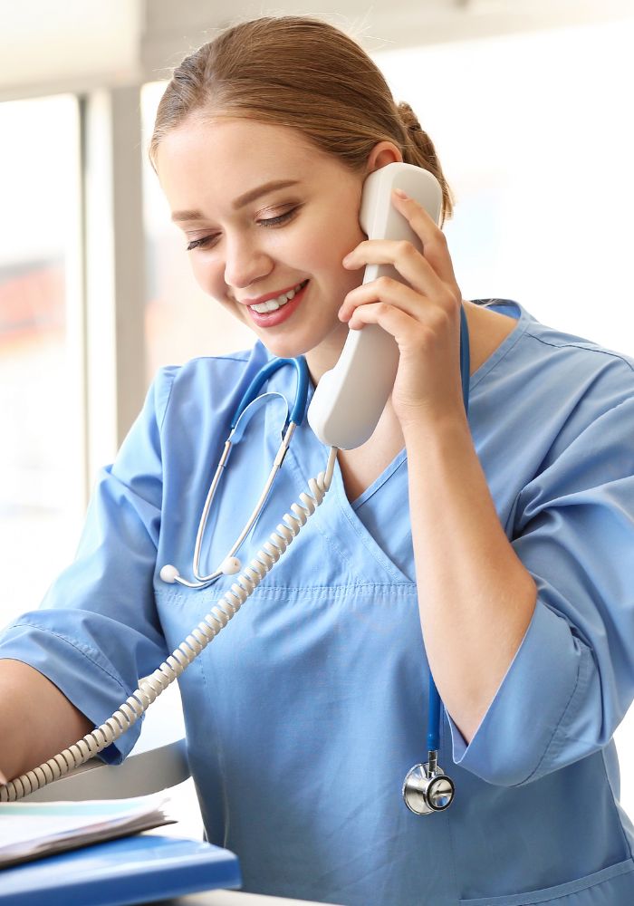 A woman wearing a blue shirt and a white stethoscope talking on a phone.