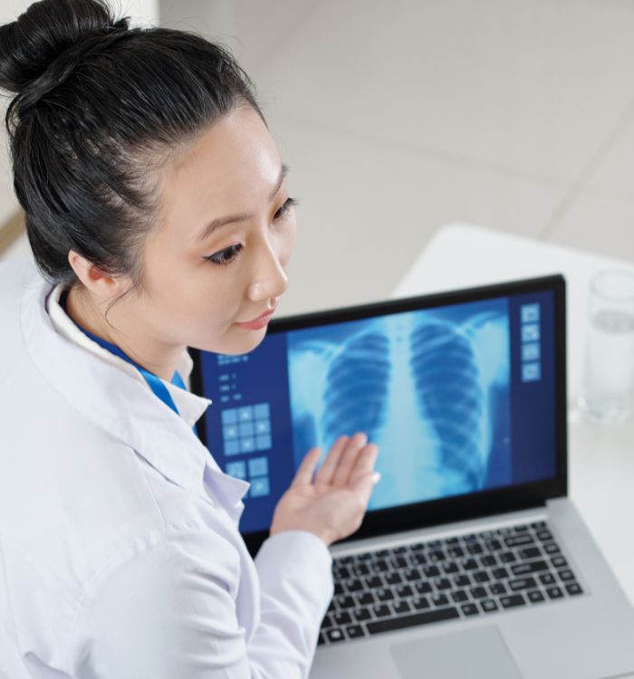 A woman in a white lab coat is pointing at a laptop screen.