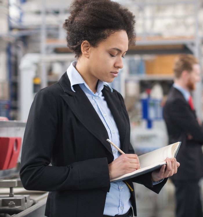 A woman in a black suit writing in a notebook.