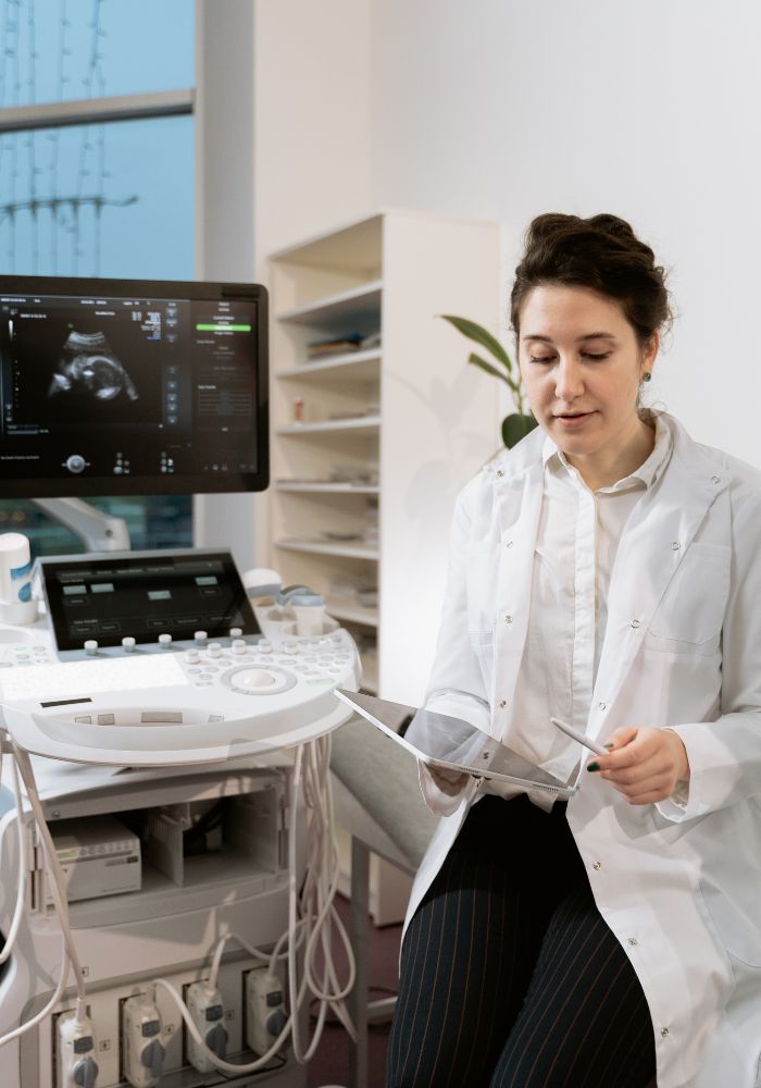 A woman in a white lab coat is looking at a computer screen.