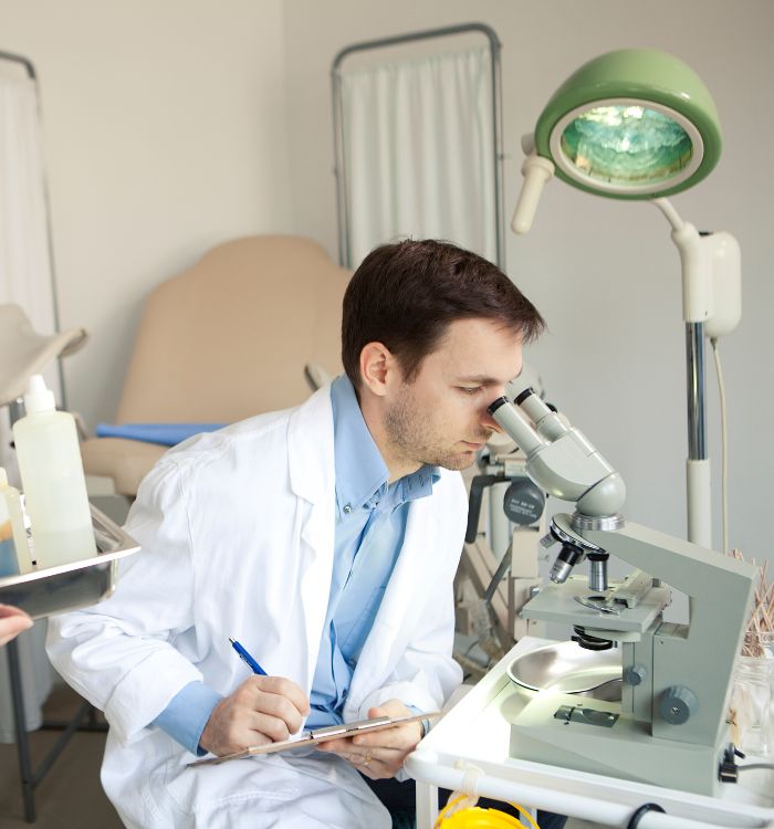 A man wearing a white lab coat is looking through a microscope.