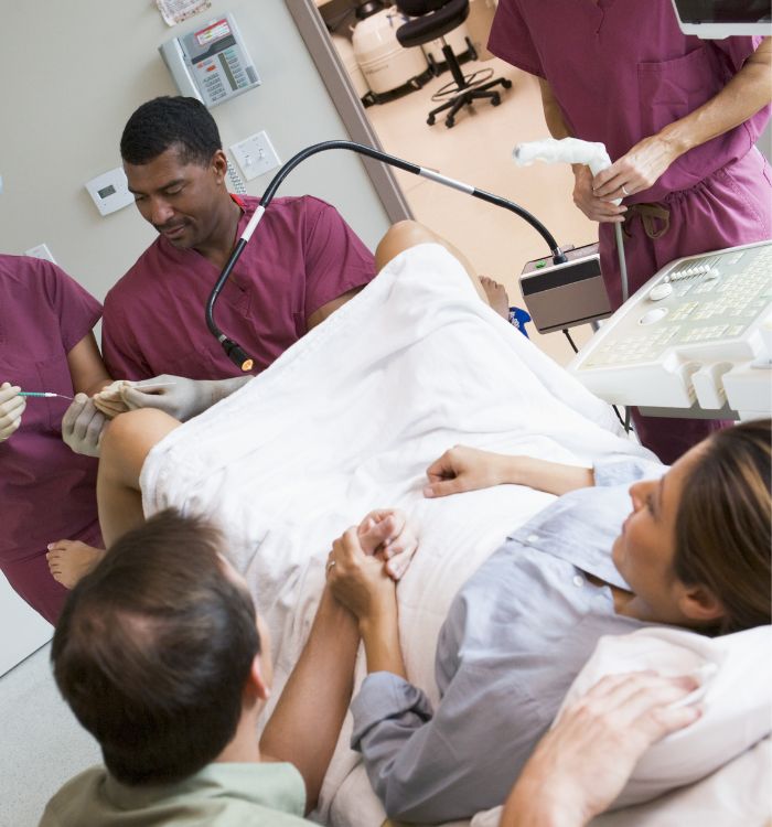 A woman is lying on a hospital bed with a man and a nurse attending to her.
