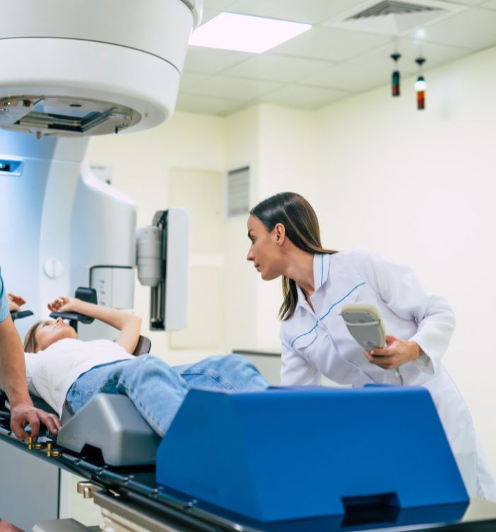 A woman in a white lab coat is standing next to a machine that is scanning a person.