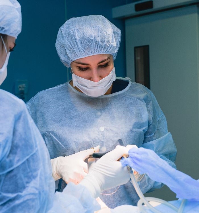 A woman wearing a blue hat and a white mask is working on a patient.
