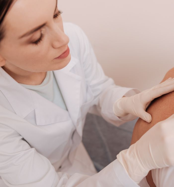 A woman in a white lab coat is applying a substance to a person's skin.