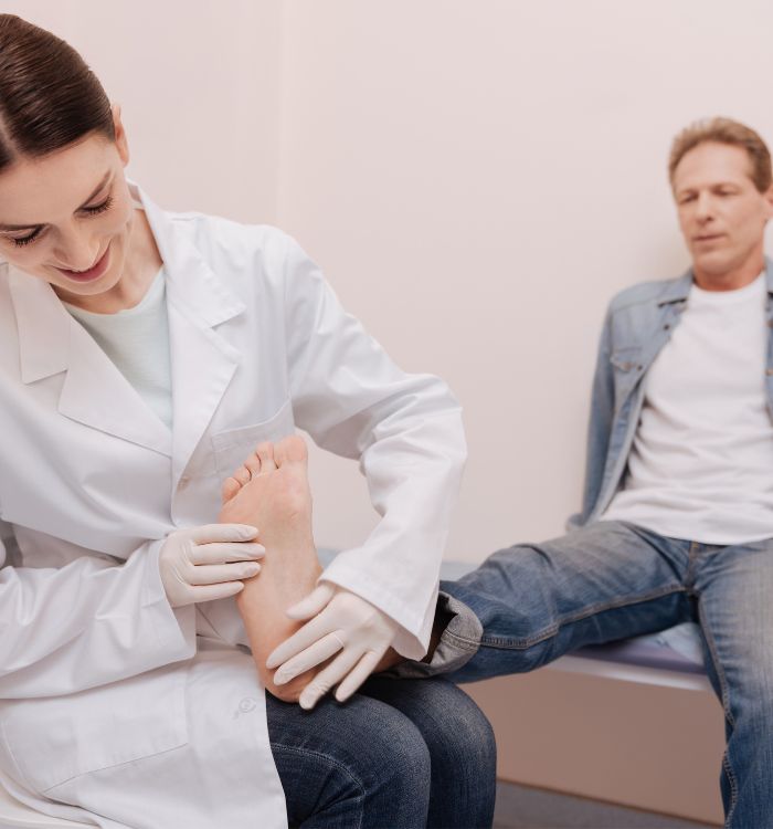 A woman in a white lab coat is massaging a man's foot.