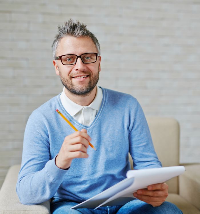 A man wearing glasses and a blue sweater is holding a pen.