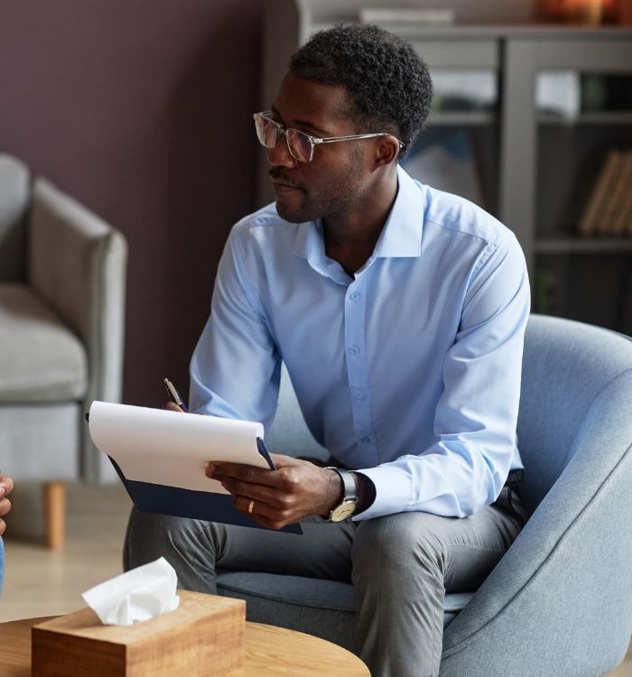 A man wearing glasses and a blue shirt is sitting in a chair.