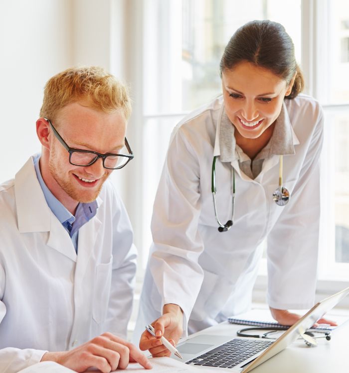 A woman in a white coat is showing a man how to use a laptop.