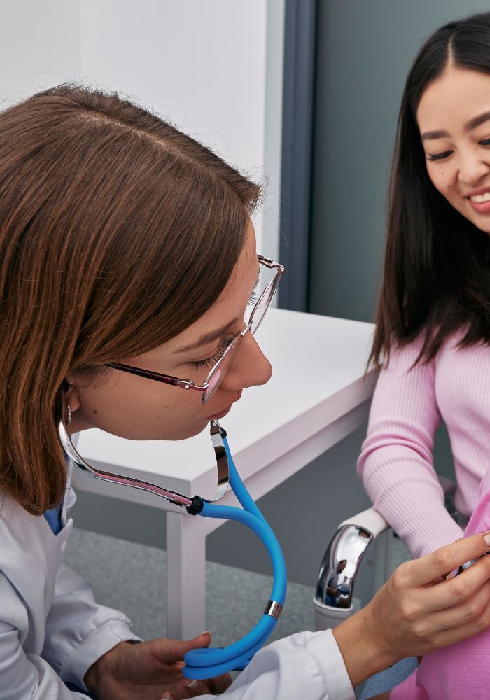 A woman wearing glasses and a stethoscope is examining a child.