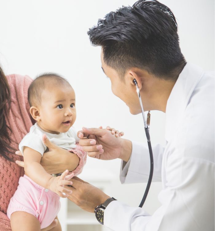 A man wearing a white shirt and a stethoscope holding a baby.