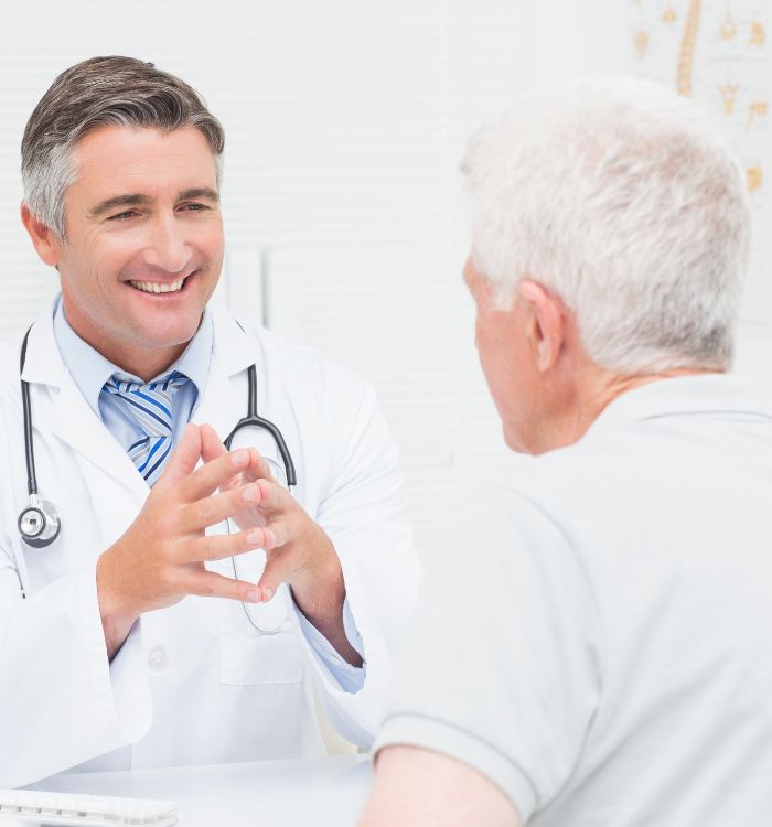 A man in a white coat is talking to an older man.