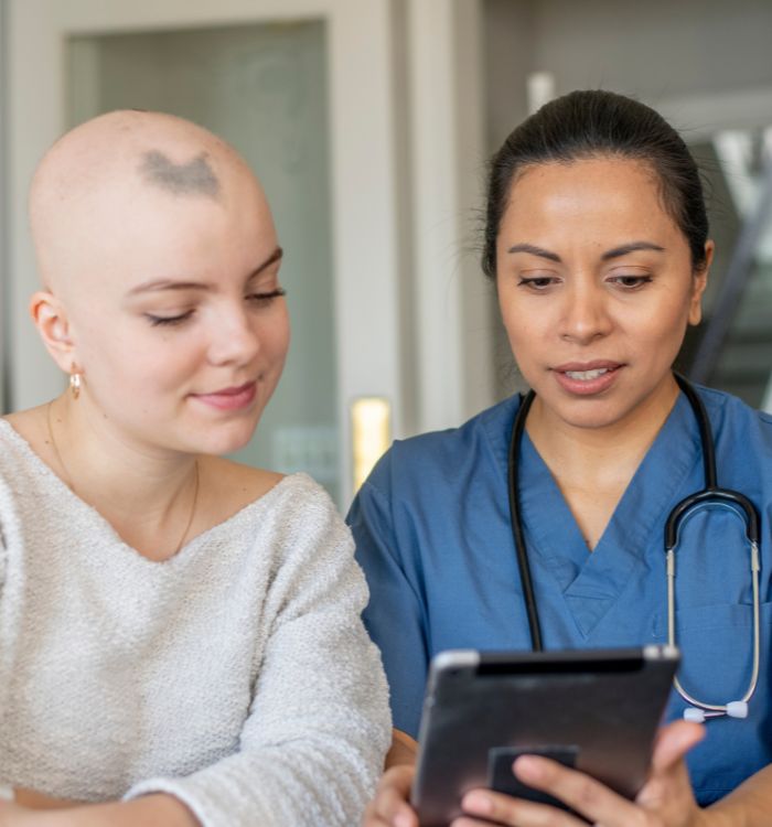 A woman with a bald head and a woman with a ponytail are looking at a tablet.