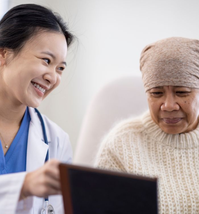 A woman in a white coat is showing a tablet to an older woman.