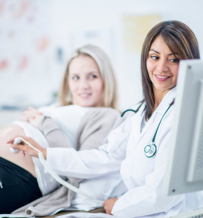 A woman in a white coat is smiling at a pregnant woman.