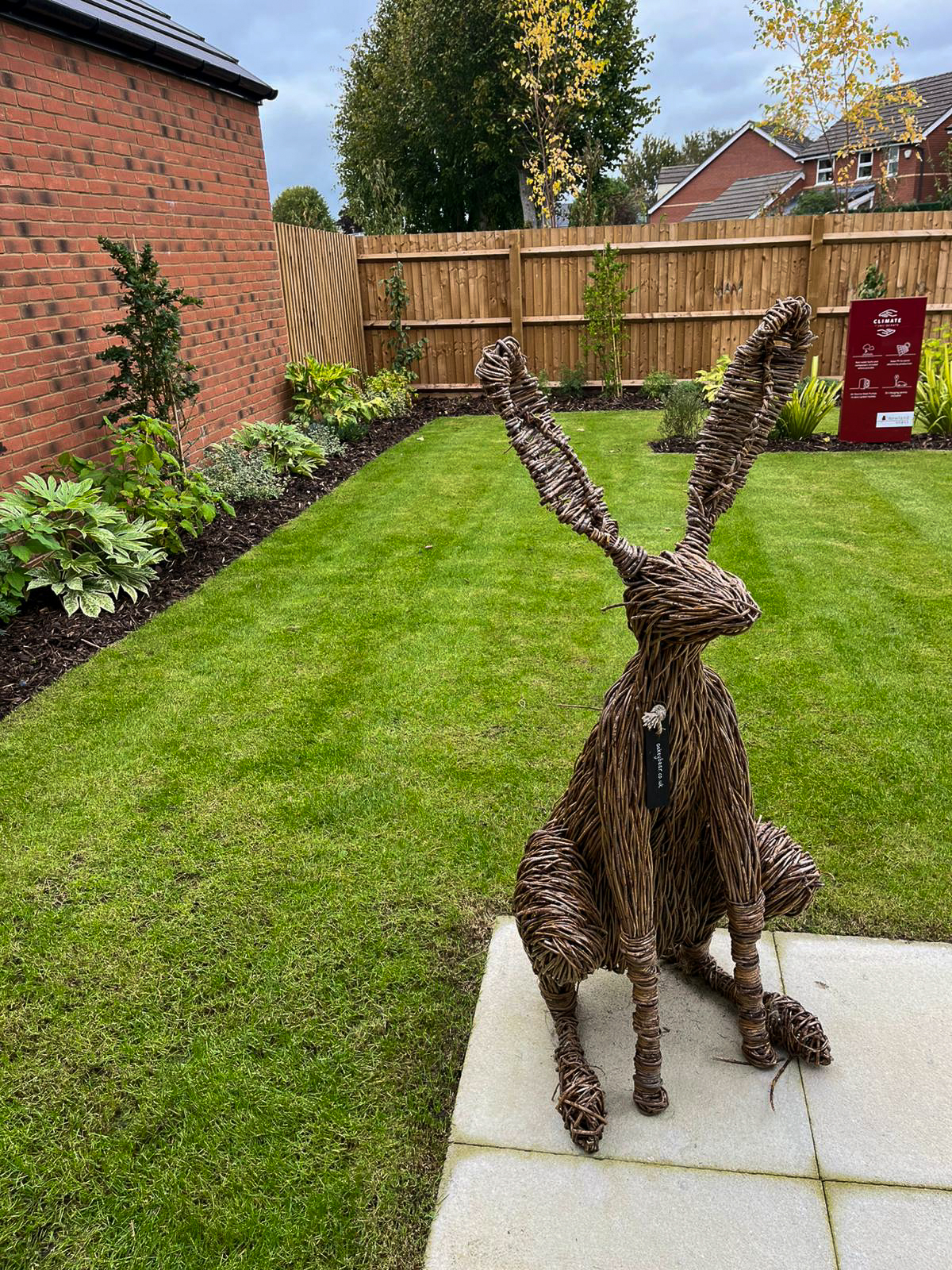 Willow hare sculpture on a patio overlooking a turfed rear garden with planted borders at Upton's Garden, Whitminster
