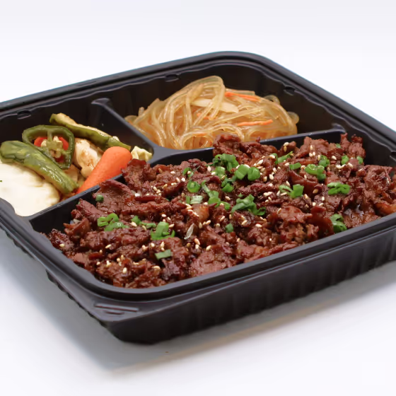 Black tray with marinated grilled beef, glass noodles, and assorted pickled vegetables.