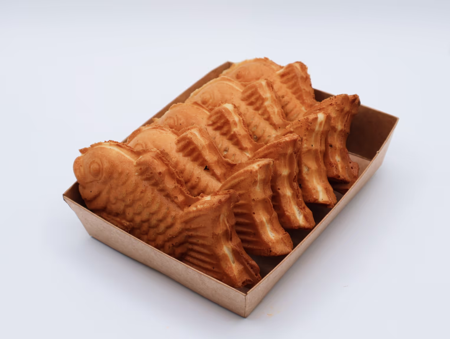 Box of six fish-shaped pastries with golden brown crust on a white surface.