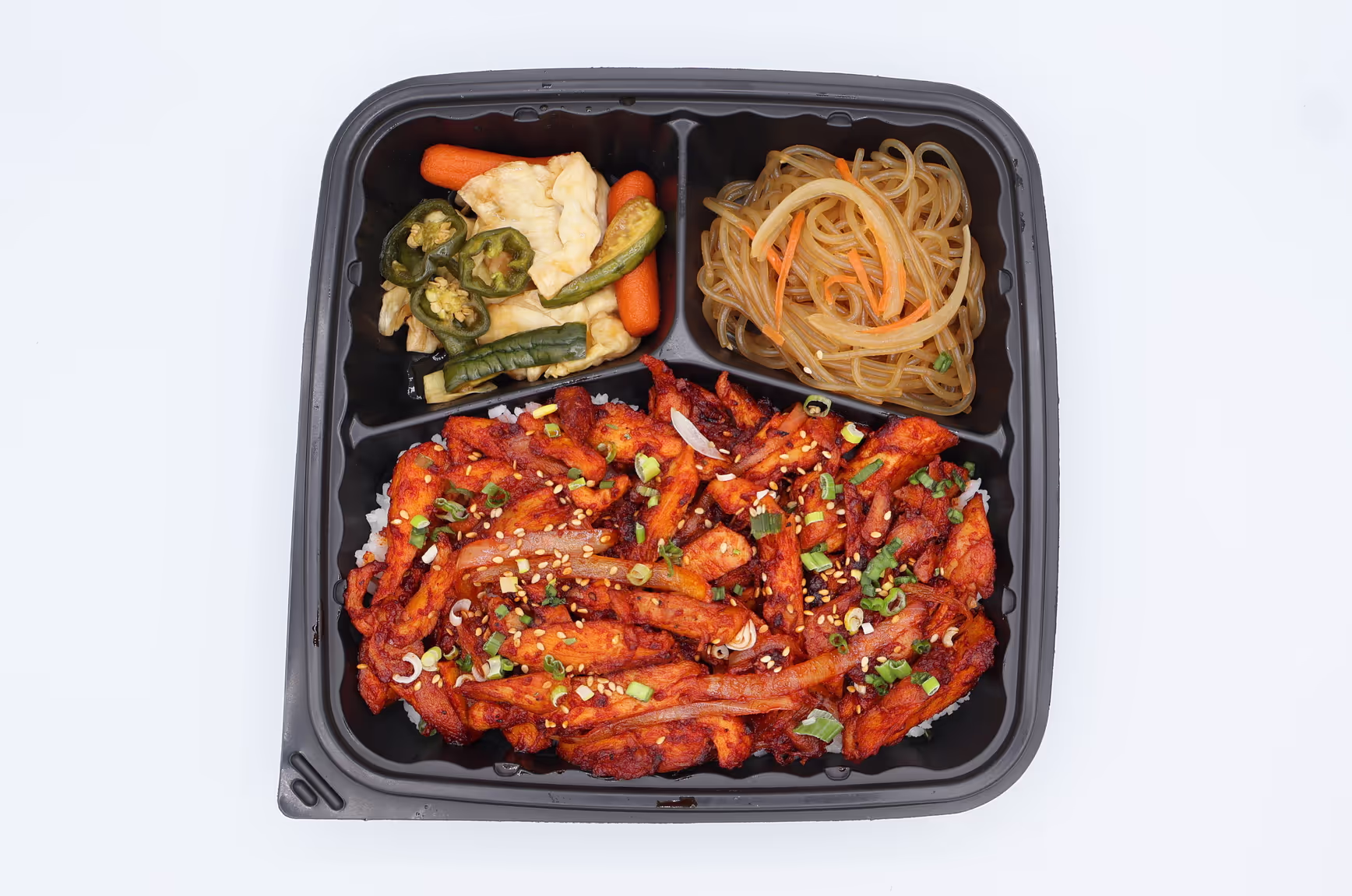 Takeout container with spicy chicken over rice, stir-fried vegetables, and glass noodles with carrots.