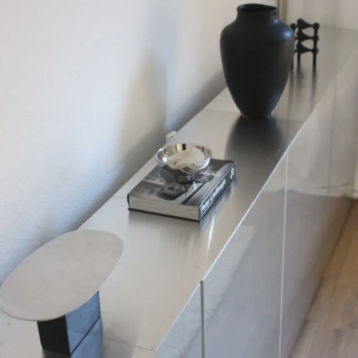 This may contain: a black vase sitting on top of a white shelf next to a book and bowl