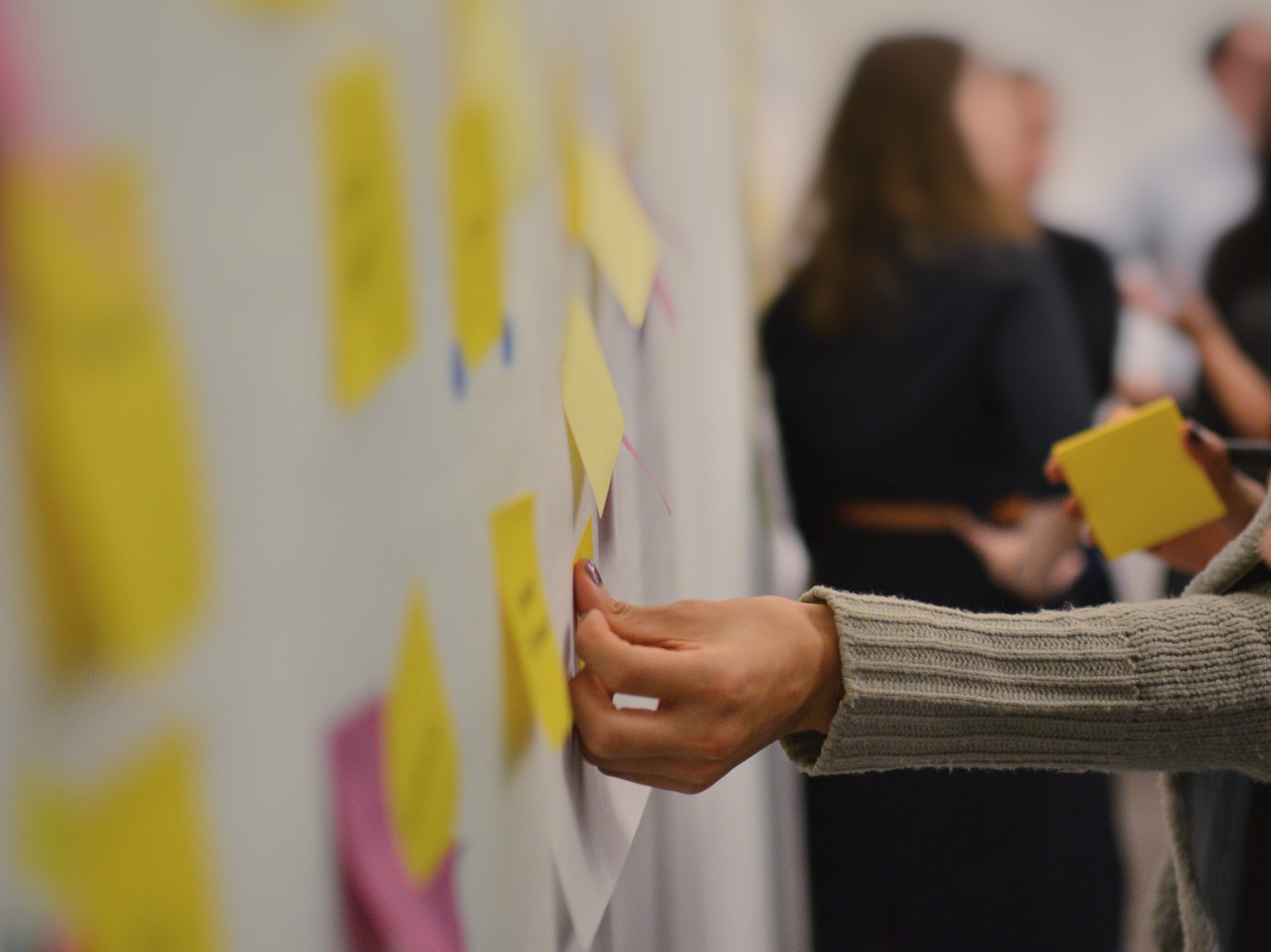 A hand putting a sticky on a white wall with other stickies. 