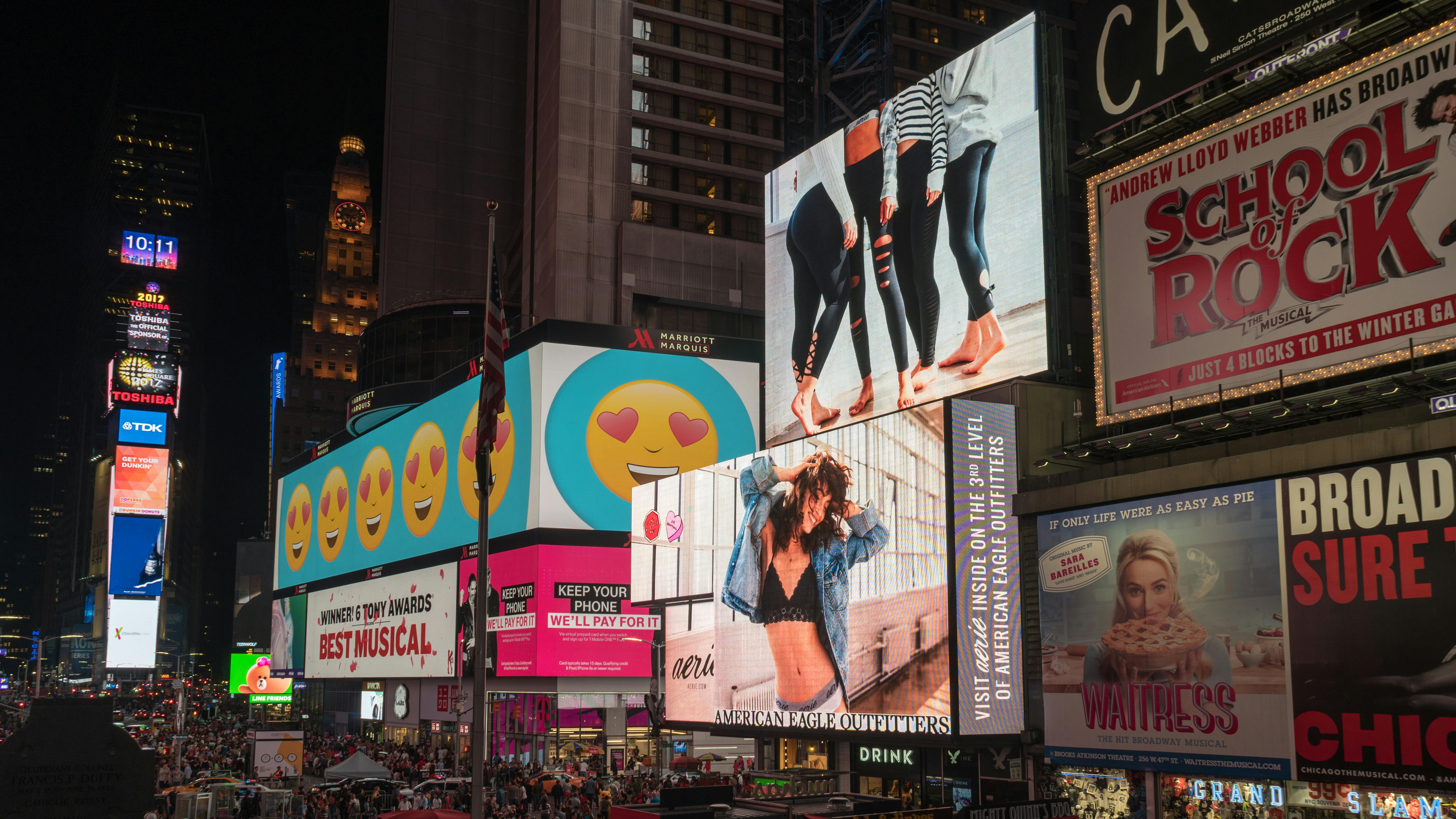 Image of Times Square in New York showing lots of lit up digital advertising billboards and people walking in the square below at night.