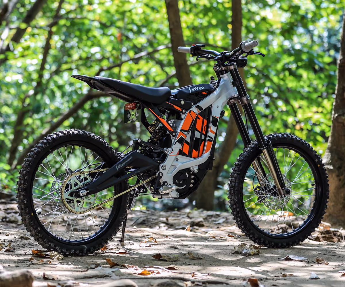 Electric dirt bike parked on a forest trail with green trees in the background.