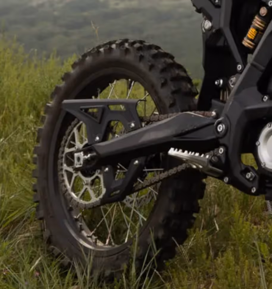 Rear wheel of a dirt bike with knobby tire and visible chain against grassy background.