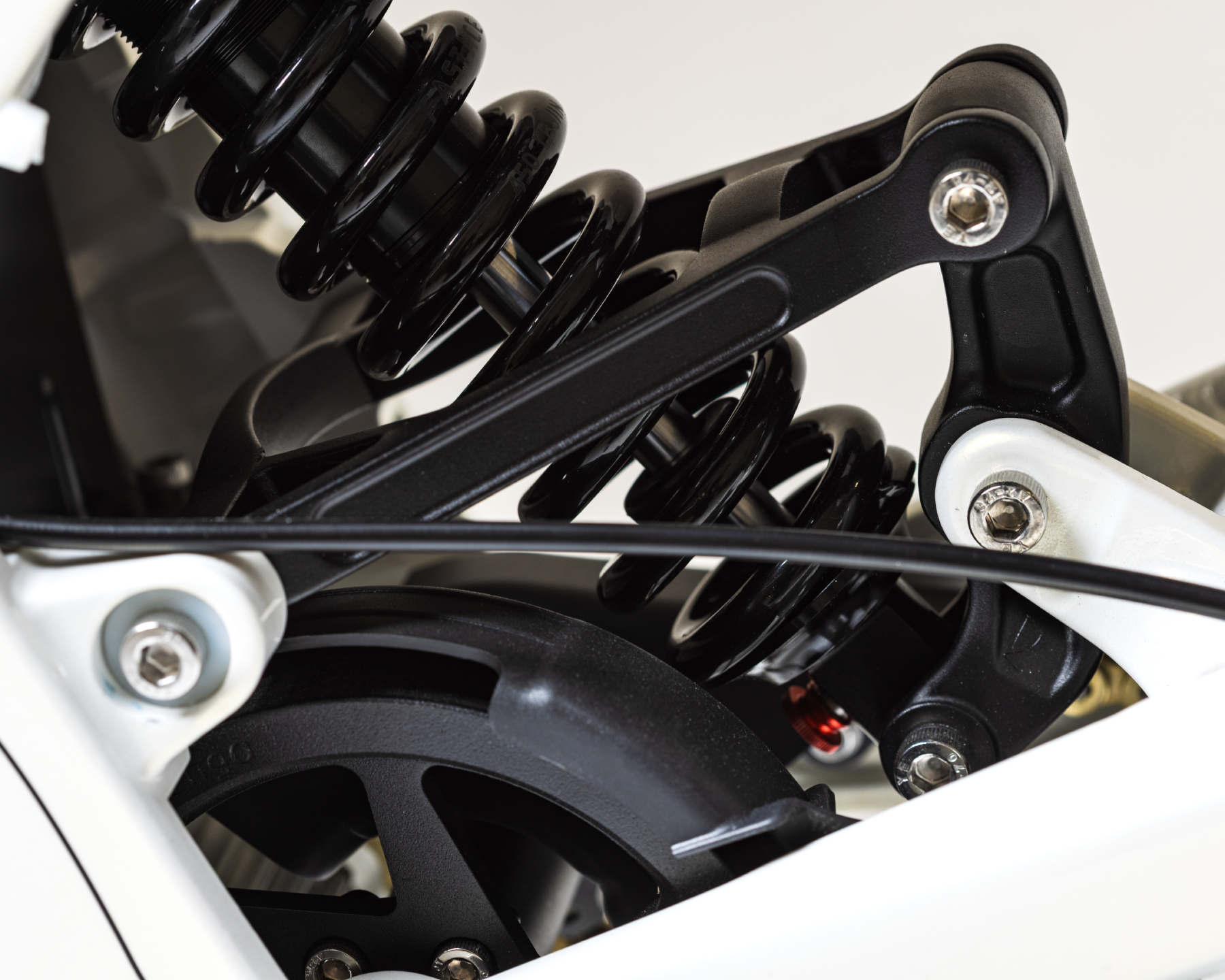 Close-up of a black coil spring suspension system on a white bicycle frame.